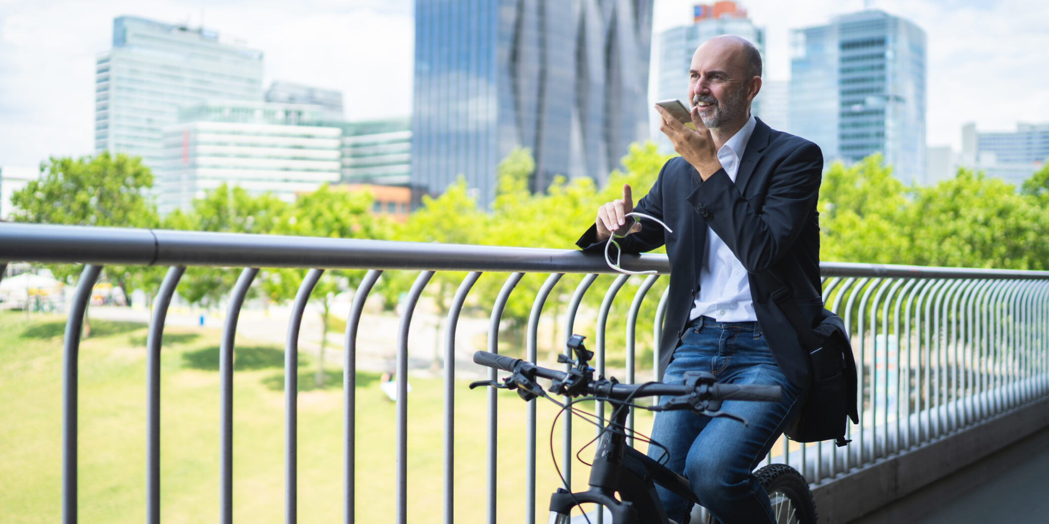friendly businessman on bicycle with smartphone in urban office district