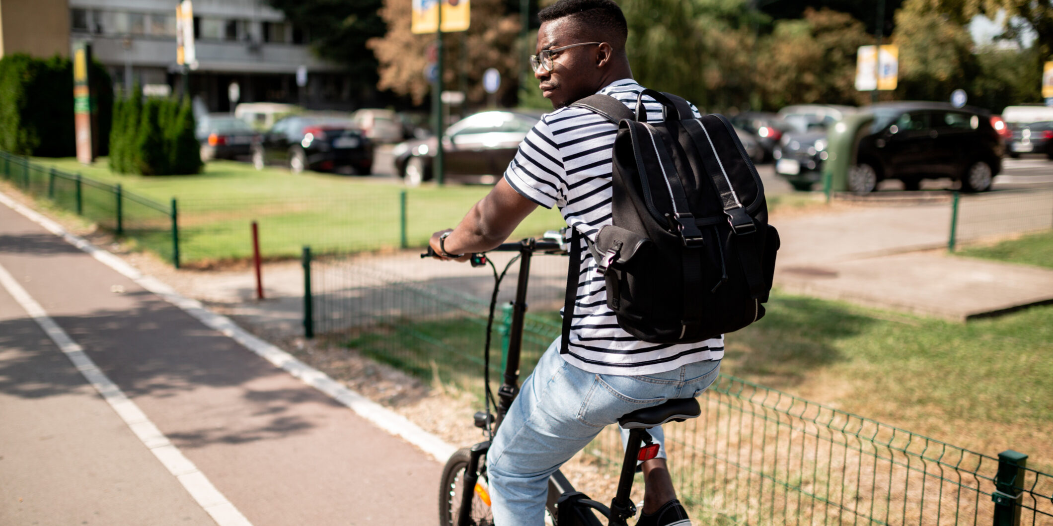 Rear view of a young African American male student riding a bicycle